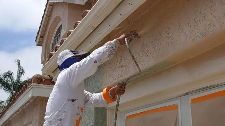 Professional painter in white protective gear and harness painting the exterior wall of a residential home in New Jersey